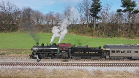 A-Drone-Slow-Motion-View-of-a-Steam-Passenger-Train,-Stopped,-Engineer-Checking-Engine,-Blowing-Smoke-on-a-Sunny-Fall-Day