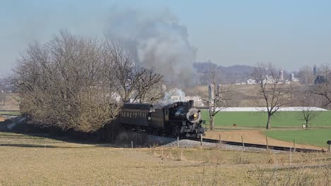 Un-Tren-De-Pasajeros-De-Vapor-Restaurado-Pasa-Soplando-Humo-Blanco-Y-Gris,-Viajando-A-Través-Del-Campo-Rural-En-Un-Soleado-Día-De-Invierno