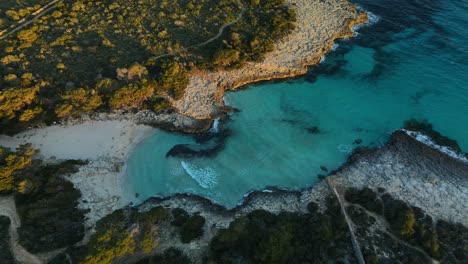 Cinematic-zoom-in-from-aerial-drone-shot-to-white-sand-beach-of-Es-talaier-in-Spain