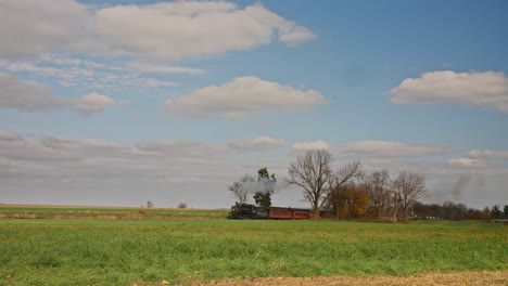 A-View-of-a-Steam-Passenger-Train-Passing-by,-Blowing-Smoke,-Traveling-Thru-Rural-Countryside-on-a-Sunny-Fall-Day