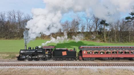 A-Drone-Slow-Motion-Close-Up-View-of-a-Steam-Passenger-Train,-Starting-Up-in-the-Countryside,-Blowing-Lots-of-Smoke-on-a-Sunny-Fall-Day
