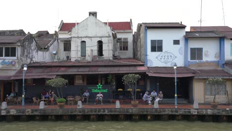 Los-Turistas-Disfrutan-Del-Ambiente-Tranquilo-Junto-Al-Café-Junto-Al-Río,-Malaca,-Malasia