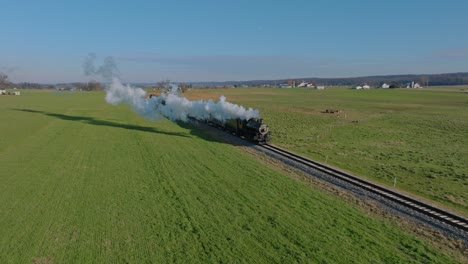 A-Drone-View-of-Cows-and-Farmlands-With-a-Single-RR-Track-and-a-Steam-Train-Approaching-Blowing-Smoke-and-Steam-on-a-Winter-Day