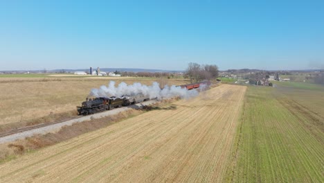 A-Slow-Motion-Drone-View-of-an-Antique-Steam-Passenger-Train,-Approaching,-Blowing-Smoke,-While-Traveling-Thru-Farmlands,-on-a-Sunny-Fall-Day