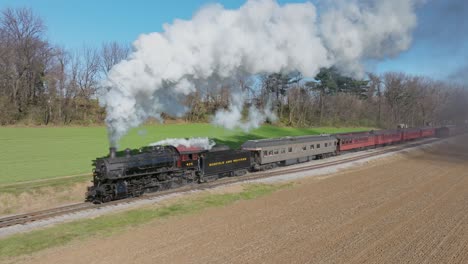 A-Drone-Slow-Motion,-Front-Angled-View-of-an-Antique-Steam-Passenger-Train,-Starts-Moving,-Blowing-Lots-of-Smoke-on-a-Sunny-Fall-Day