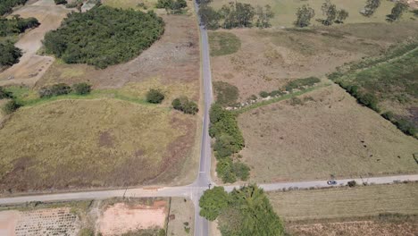 Countryside-city-road-with-overgrown-crossroads-with-lone-car-passing-by-aerial-view