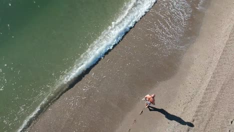 Aerial-views-over-a-beach-with-gentle-waves-and-people-walking-along-the-shore-calmly