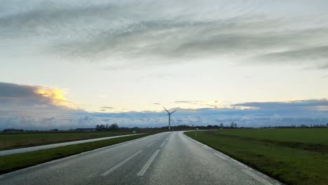Windmühle-In-Der-Ferne-Mit-Sonnenaufgang-Und-Herannahenden-Autos-Auf-Der-Straße
