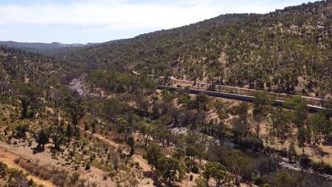 Vista-Aérea-Del-Tren-De-Pasajeros-Del-Pacífico-Indio-Que-Sale-A-Través-De-Las-Colinas-De-Perth