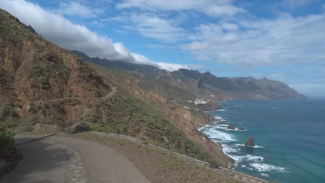 Timelapse-Of-A-Coastal-Shoreline-Road-With-Tall-Mountains,-Blue-Sky-And-Fast-Moving-Clouds,-Tenerife,-Spain
