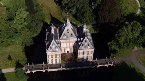 Panning-drone-shot-of-the-lavish-Duivenvoorde-Castle,-one-of-the-oldest-castles-in-South-Holland,-surrounded-by-lush-green-trees
