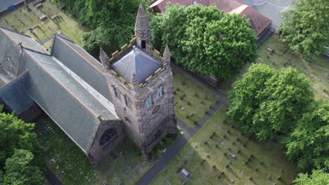 Aerial-view-above-rural-English-town-woodland-countryside-idyllic-church-rooftop-and-graveyard