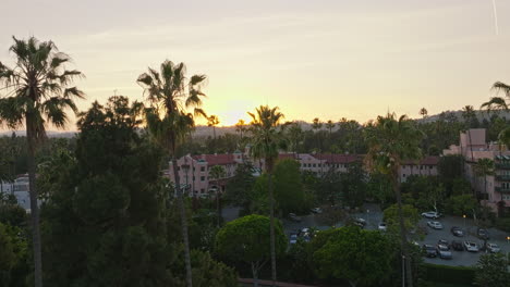 Flying-Through-Palm-Trees-Towards-the-Historic-Pink-Beverly-Hills-Hotel,-Gorgeous-Chateau-in-the-Warm-Sunset