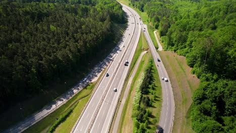 Drone-birds-eye-shot-showing-traffic-on-asphalt-highway-surrounded-by-green-dense-woodland