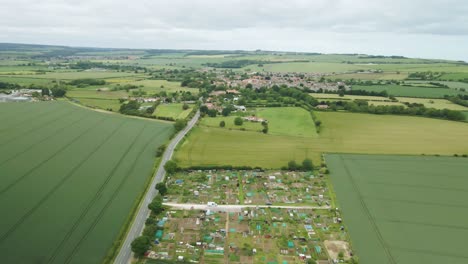aerial-of-rural-English-countryside-with-allotments,-fields-and-village-in-background