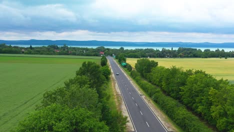 car-comes-from-the-lake-on-the-highway-with-beautiful-rainy-background,-drone-footage