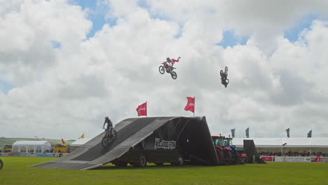 Das-Freestyle-Motocross-Stunt-Display-Team-Führt-Beim-Big-Jump-Event-Der-Royal-Cornwall-Show,-Großbritannien,-Fliegende-Tricks-In-Der-Luft-Vor-–-Weitwinkelaufnahme-In-Zeitlupe