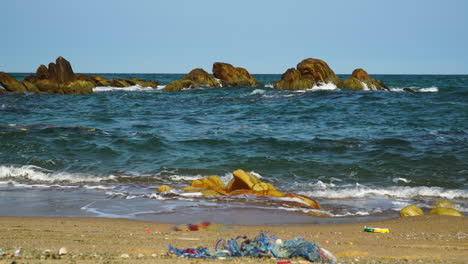 Statische-Aufnahme-Mehrerer-Plastikgegenstände,-Die-Am-Meeresufer-Liegen-Bleiben,-Während-Die-Meereswellen-Brechen