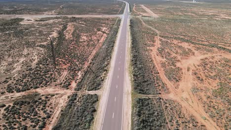 Drohnenaufnahmen-über-Einer-Landwüstenstraße-In-Australien,-Schwenk-Nach-Oben,-Um-Windparks-Mit-Erneuerbarer-Energie-Zu-Enthüllen
