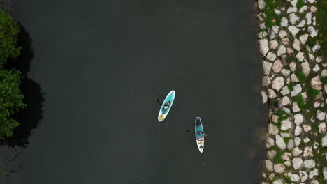 People-paddle-boarding-on-the-river-with-rocks-wall-on-one-side-of-the-river