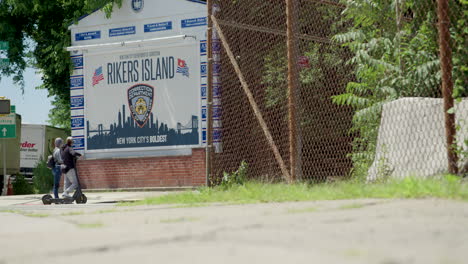 People-On-Electric-Scooters-Stop-In-Front-Of-Rikers-Island-Jail-Sign-In-NYC