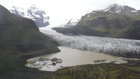 Plano-Amplio-Del-Glaciar-De-Islandia-Con-Agua,-Hierba-Verde-Y-Hielo-Azul-Con-Video-De-Drones-Moviéndose-Hacia-Abajo