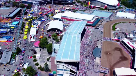 Luftüberführung-Calgary-Stampede-Fair-Mit-Blick-Auf-Pferderennen-Von-Den-Tribünen-Bis-Hin-Zu-Den-Menschenmassen,-Die-Sich-An-Einem-Strahlend-Sonnigen-Nachmittag-Zum-Essen-Und-Für-Lustige-Fahrgeschäfte-Anstellten