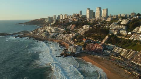 Aerial-view-flying-across-Reñaca-affluent-cityscape-resort-waterfront-and-golden-beach-coastline