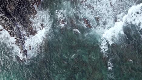Aerial-view-from-above-of-Pacific-Ocean-water-crashing-against-the-shore-of-a-Hawaiian-island,-creating-a-beautiful-texture