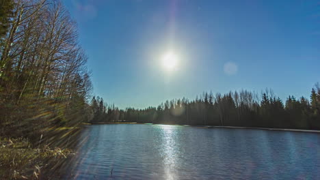 Static-view-of-sun-rising-in-timelapse-over-pristine-lake-surrounded-by-tree-forest-during-spring-time-throughout-the-day