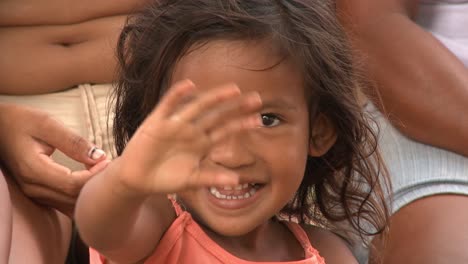 Primer-Plano-De-Una-Joven-Indígena-Amazónica-Sentada-Con-Sus-Padres-Sonriendo-Y-Saludando-Hola