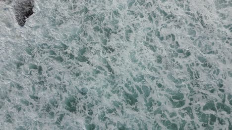 Top-down-aerial-view-of-foamy-ocean-waves-hitting-the-rocks