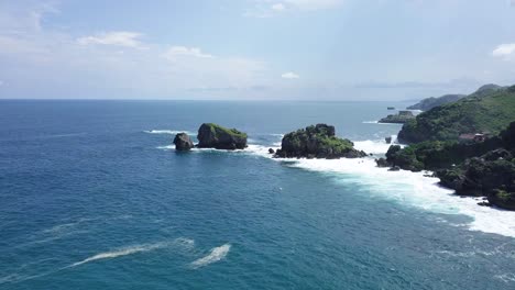 Drone-shot-of-two-rock-island-on-the-beach,hit-by-waves-during-sunny-day---TIMANG-ISLAND,-YOGYAKARTA,-INDONESIA
