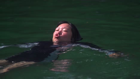 Asiatische-Frau-Trägt-Badeanzug-Und-Schwimmt-Im-Flusswasser,-Während-Sie-Niedliche-Gesichter-Macht,-Gefilmt-In-Zeitlupe
