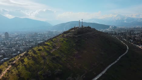 Luftaufnahme-Des-Grünen-Calan-Hügelwanderwegs-Und-Des-Observatoriums-Auf-Dem-Gipfel,-Stadt-Und-Berge-Im-Hintergrund,-Santiago,-Chile