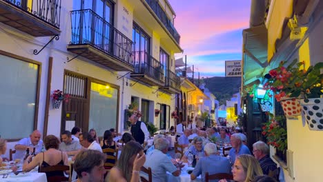 People-sitting-and-having-dinner-outside-in-a-restaurant-with-a-beautiful-sunset-pink-sky-in-Benahavis-Spain,-romantic-street-in-the-evening-during-summer,-4K-shot