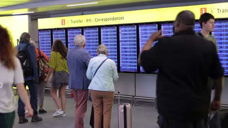 Pareja-Mayor-Comprobando-La-Información-Del-Vuelo-En-El-Tablero-Digital,-Aeropuerto-Charles-De-Gaulle