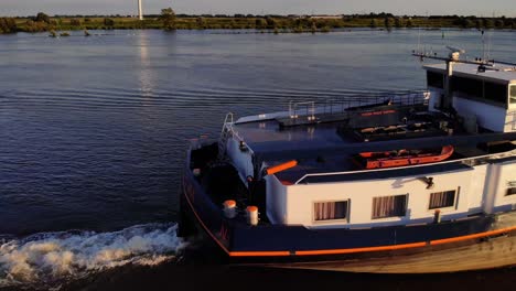 Aerial-Close-Up-View-Of-Stern-Of-FPS-Waal-Inland-Cargo-Vessel-Along-Oude-Maas-With-During-Golden-Hour