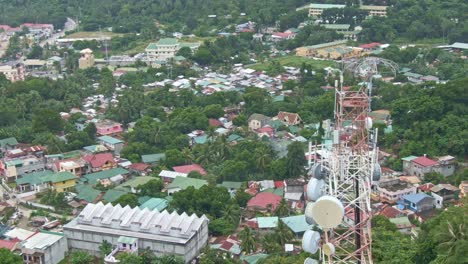 Aerial-drone-view-of-signal-tower,-houses-and-buildings-surrounded-by-trees-from-Puerto-Galera,-Philippines
