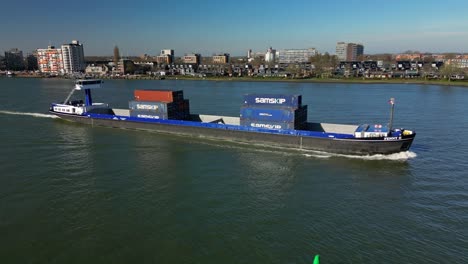 Toma-Aérea-De-Un-Barco-De-Transporte-Con-Contenedores-Que-Navegan-Hacia-La-Ciudad-De-Dordrecht,-Países-Bajos