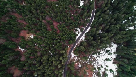 Car-on-the-curvy-road-cutting-through-the-evergreen-alpine-forest-in-winter