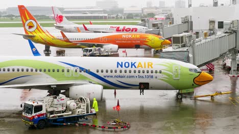 Nokair-Und-Thai-Lion-Airlines-Legen-An-Einem-Regnerischen-Tag-Am-Don-Mueang-International-Airport-DMK-In-Der-Halle-An,-Während-Sie-Sich-Mit-Bodenpersonal-Auf-Den-Abflug-Vorbereiten