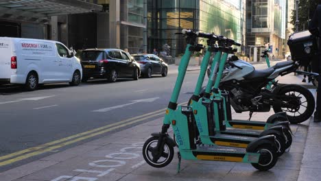 London-Canary-Wharf-Aug-2022-row-of-electric-scooters-wait-for-use-by-side-of-road