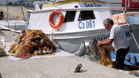 Man-mending-orange-fishing-nets-on-moored-boat-in-sozopol-marina-harbour