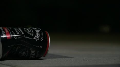 static-shot-of-a-falling-crushed-jack-daniels-can-on-the-ground-during-the-night-in-slow-motion