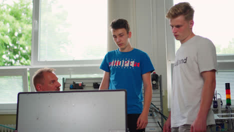 Male-Teacher-Explaining-How-To-Use-A-Miniature-Conveyor-Belt-Sorting-Machine-To-Two-Vocational-Students-In-Slovakia---medium-shot