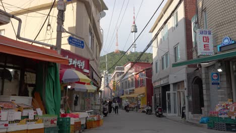 Atmospheric-Yongsan-Haebangchon-Village-narrow-street-with-N-Seoul-Namsan-Tower-view-and-local-old-style-shops,-people-sightseeing