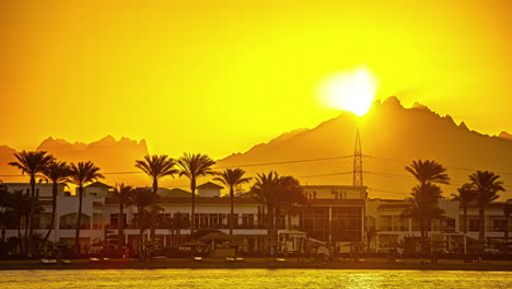 Bright-Orange-Sun-Rising-Behind-The-Mountain-During-Sunsrise-With-Oceanfront-Buildings-In-The-Foreground