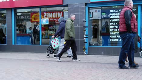 Slow-motion-troubled-shoppers-walking-in-British-retail-high-street-struggling-with-cost-of-living-budget-spending-crisis