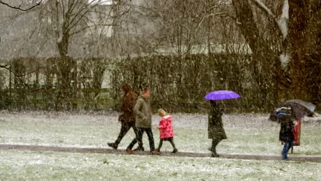 Parents-walking-kids-to-school-in-blizzard-snow-cold-weather-in-windy-UK-winter-storm-conditions